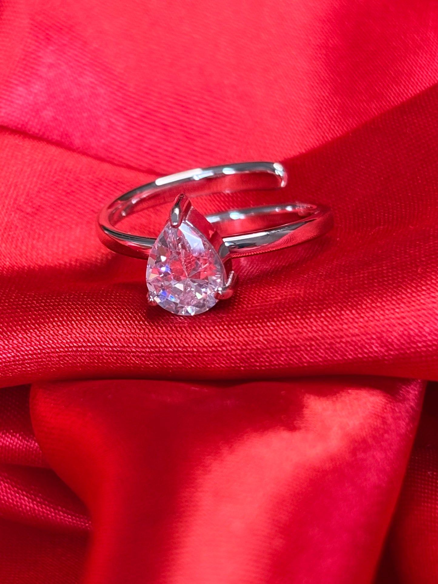 Heart's Desire Ring with a pear-cut gemstone on a silver band against red satin.