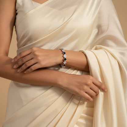 Aurevia Fashion Jewellery tennis bangle with black clover motifs and sparkling stones worn on a woman in a cream saree