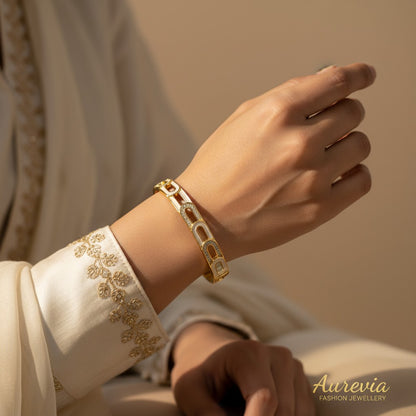 Aurevia Fashion Jewellery gold-tone link bangle with cubic zirconia stones worn on a woman's wrist in cream clothing.