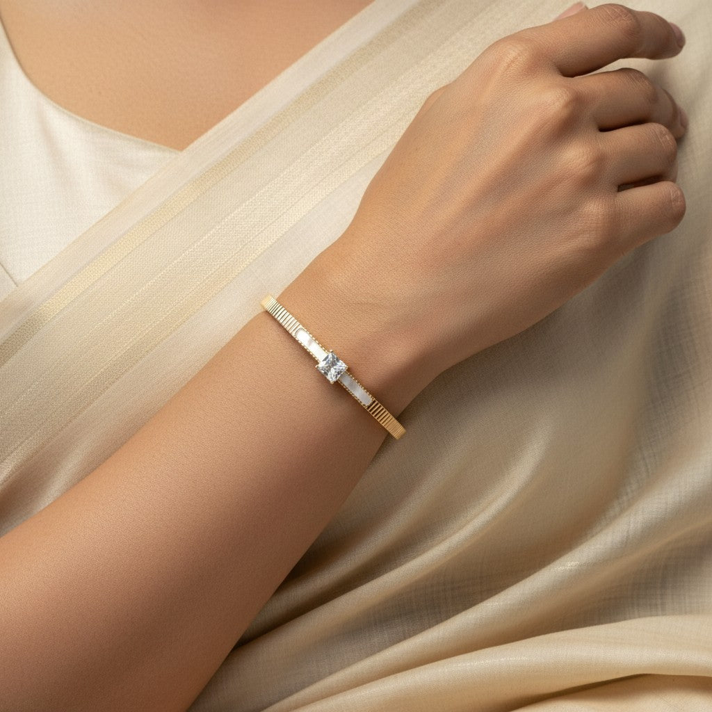 Aurevia Fashion Jewellery gold-tone cuff bangle with a sparkling princess cut center stone worn on a woman's wrist.