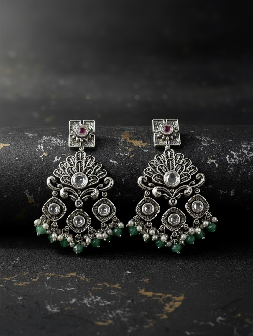 Aurevia Fashion Jewellery Jhansi Regal silver-toned drop earrings with intricate filigree, pink stones, and green beads.