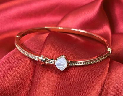 Aurevia Fashion Jewellery gold-tone bangle featuring a mother of pearl shell inlay and starfish accent on red satin.