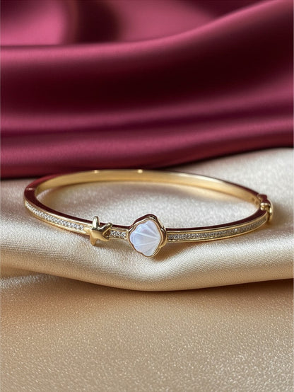 Aurevia Fashion Jewellery gold bangle featuring a mother of pearl shell and starfish charm on a satin background.