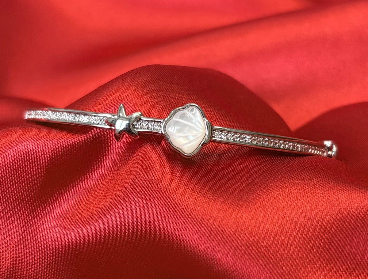 Aurevia Fashion Jewellery bangle featuring a mother of pearl shell inlay and a starfish charm on a red satin fabric.