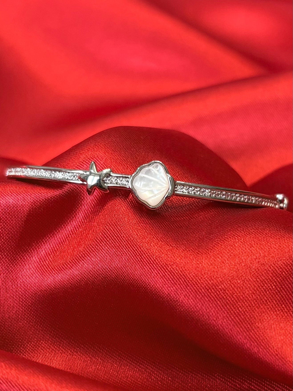 Aurevia Fashion Jewellery bangle featuring a mother of pearl shell and starfish charm on a red satin background