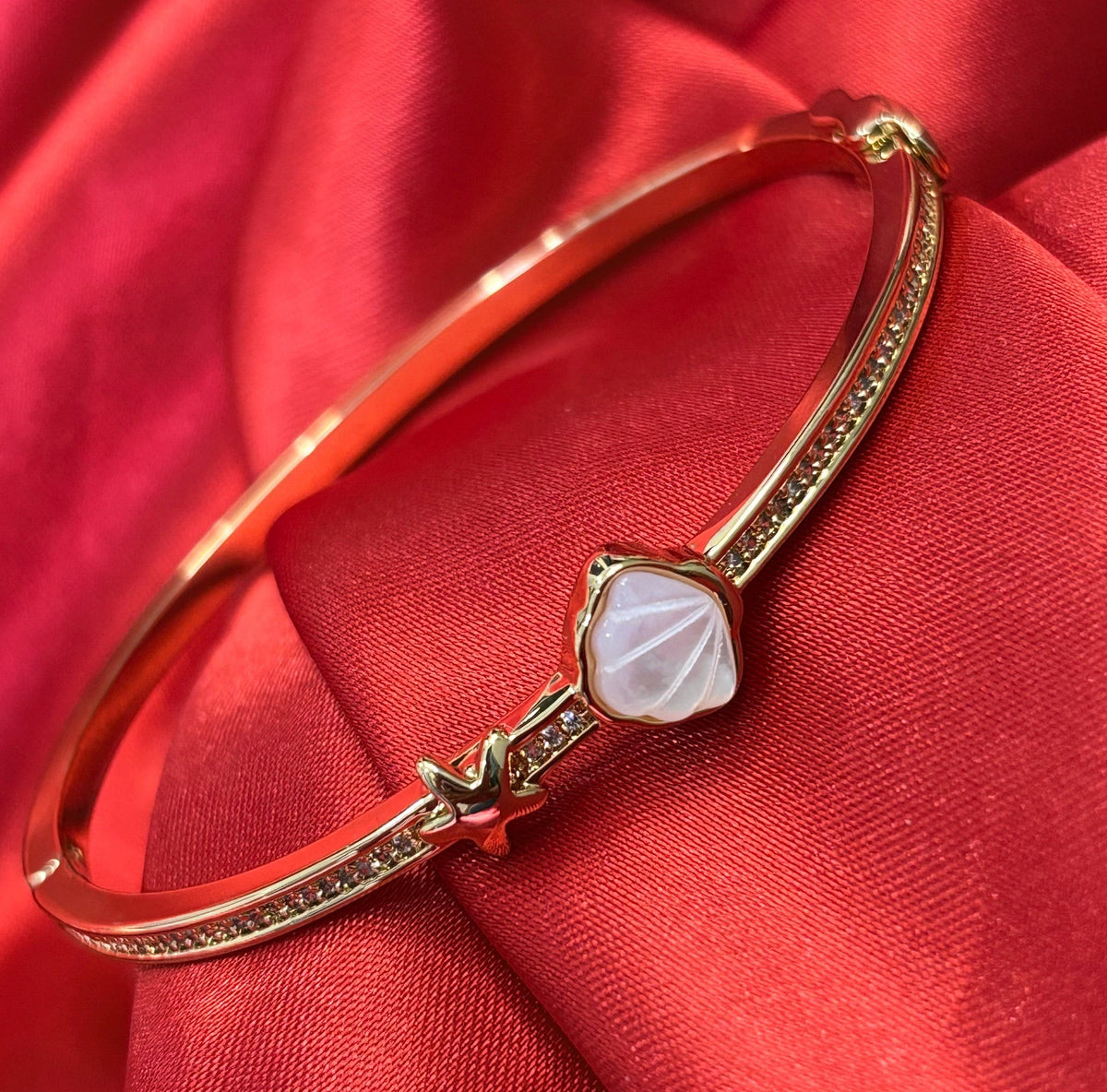 Aurevia Fashion Jewellery gold-tone bangle featuring a mother of pearl shell inlay and a small starfish accent.