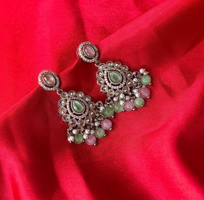 Aurevia Fashion Jewellery Noor multi-color kundan drop earrings with pastel gemstones on a vibrant red silk background.