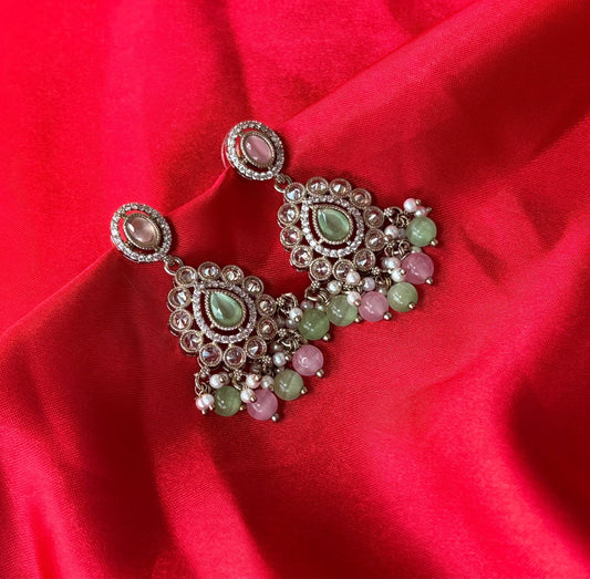 Aurevia Fashion Jewellery Noor multi-color kundan drop earrings with pastel gemstones on a vibrant red silk background.