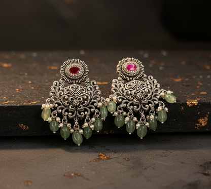 Aurevia Fashion Jewellery Jhansi Grace oxidized silver earrings with red stones, green beads, and pearl accents.