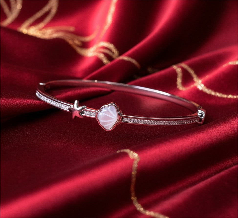 Aurevia Fashion Jewellery bangle featuring a mother of pearl shell and starfish charm on a red satin background.