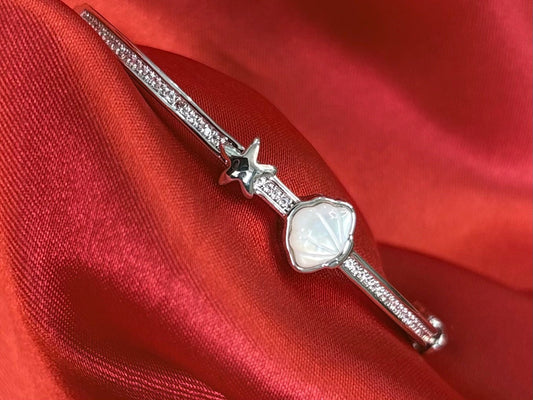 Aurevia Fashion Jewellery bangle featuring a mother of pearl shell and starfish charm on a crystal-encrusted band.